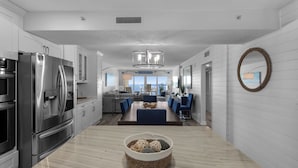 A modern kitchen with stainless steel appliances, a dining area with blue chairs, and a view of the ocean through large windows. - Sandy Key 816: 2 BR/2 BA Perdido Key Beachfront Condo, On-Site Rental Office, Sleeps 6 (Pensacola)