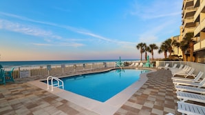 A pool area with a view of the ocean, surrounded by lounge chairs and palm trees. - Sandy Key 816: 2 BR/2 BA Perdido Key Beachfront Condo, On-Site Rental Office, Sleeps 6 (Pensacola)