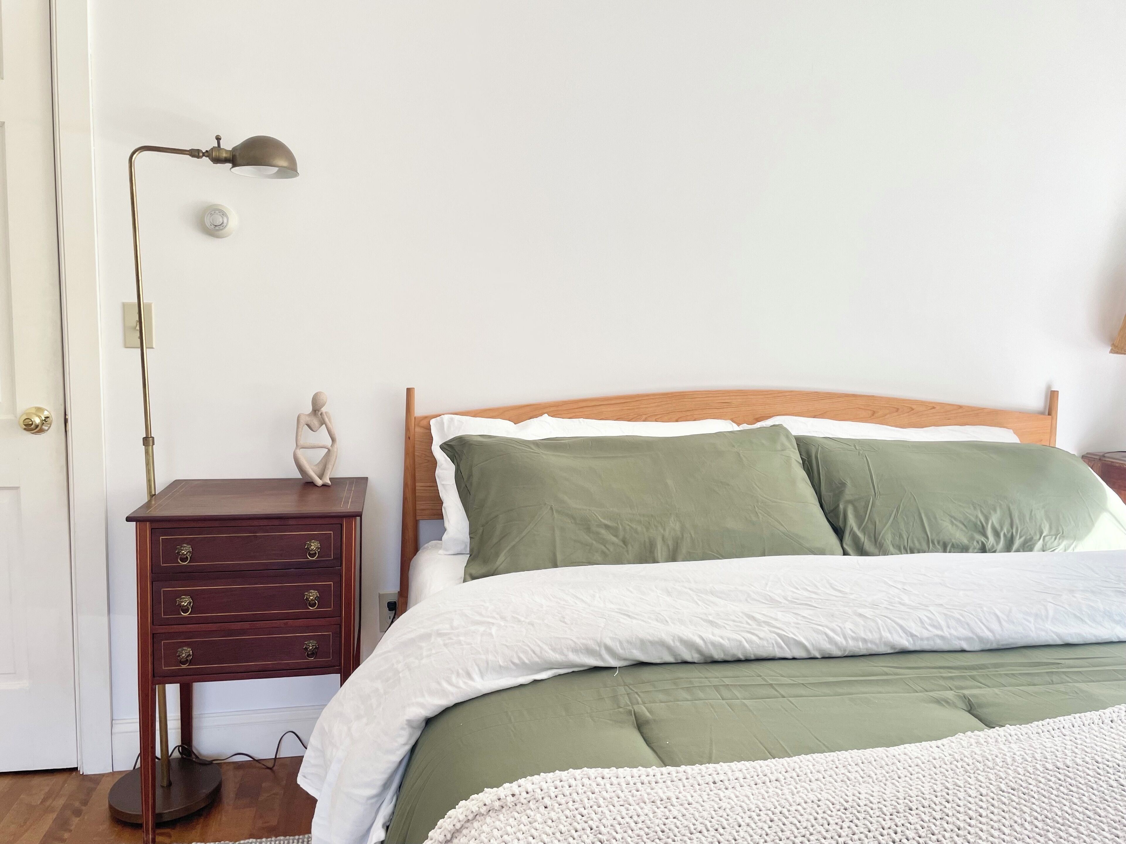 Une chambre à coucher avec un lit en bois, une literie verte et blanche, une table de chevet avec des tiroirs et une lampe de sol.