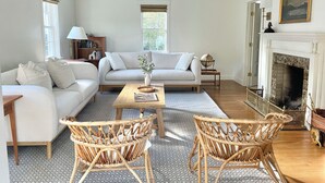 Un salón amplio con un sofá, dos sillones de mimbre, una mesa de centro y una chimenea.