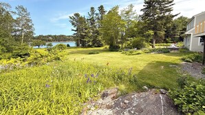 Un jardín bien cuidado con diversas plantas y flores, una gran roca al frente y un lago en el fondo.