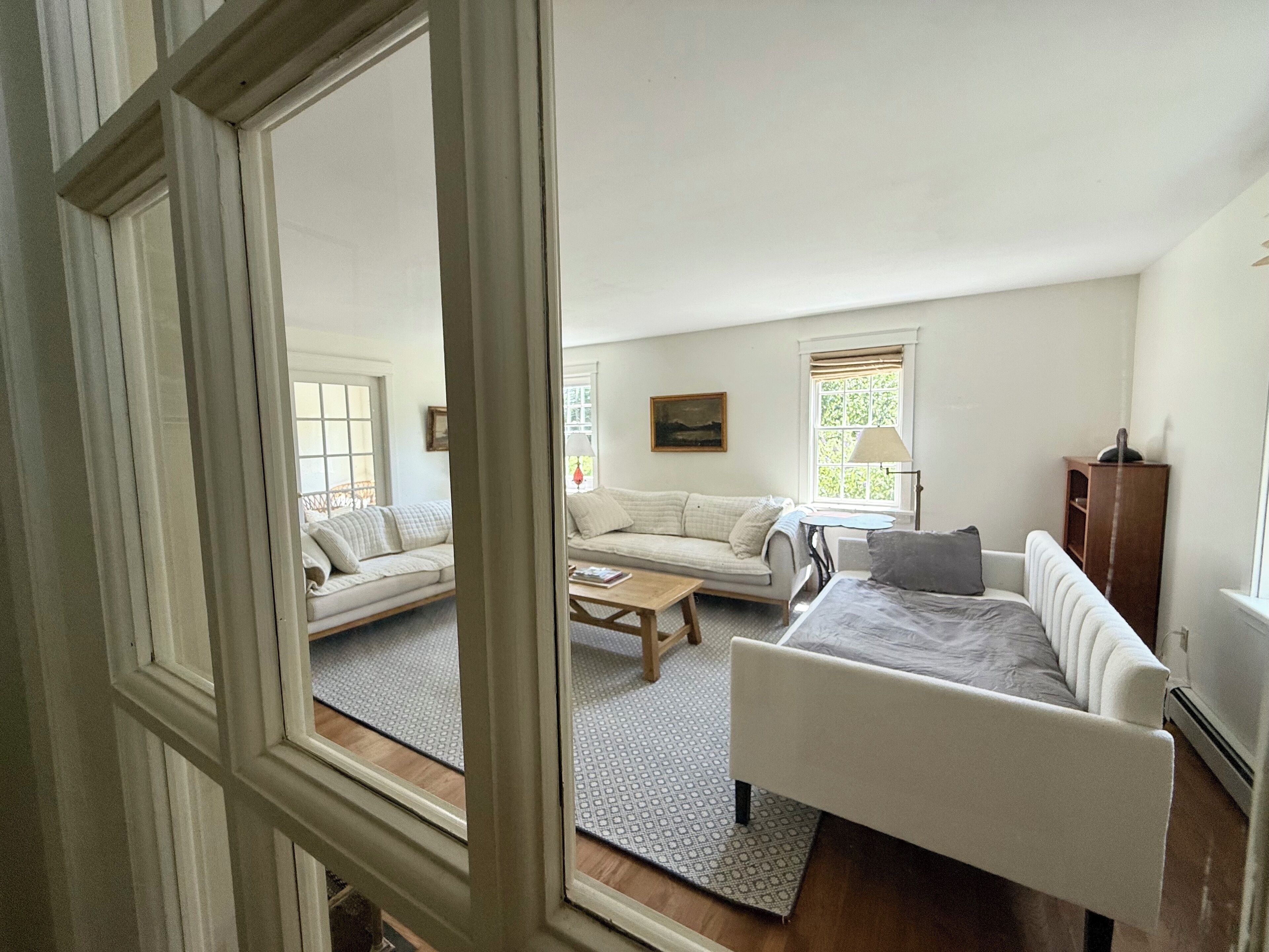 Un salon avec un canapé, une table basse et un lit. Il y a une fenêtre avec des stores et une lampe sur une table d’appoint.