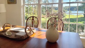 Una mesa de comedor con una cesta tejida, un jarrón con flores y un cuadro en la pared.