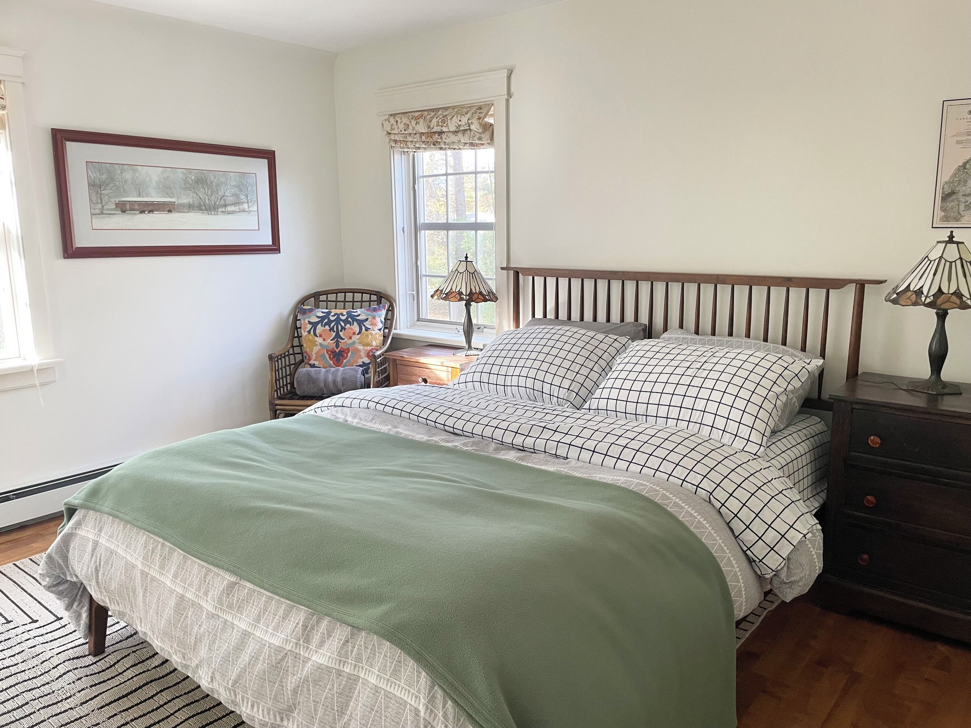 A bedroom with a bed, a chair, a nightstand, a lamp, and a window with curtains.