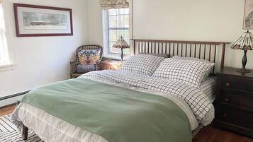 A bedroom with a bed, a chair, a nightstand, a lamp, and a window with curtains.