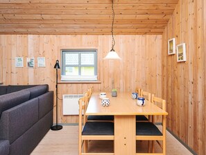 Une pièce avec un plancher en bois, un canapé, une table à manger avec des chaises, une fenêtre avec des stores et une lampe.