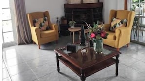 Un salon avec deux fauteuils jaunes, une table basse en bois, une cheminée et un luminaire suspendu.
