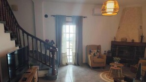 Un salon avec un escalier en bois, un téléviseur à écran plat, une cheminée et une grande fenêtre avec des rideaux.