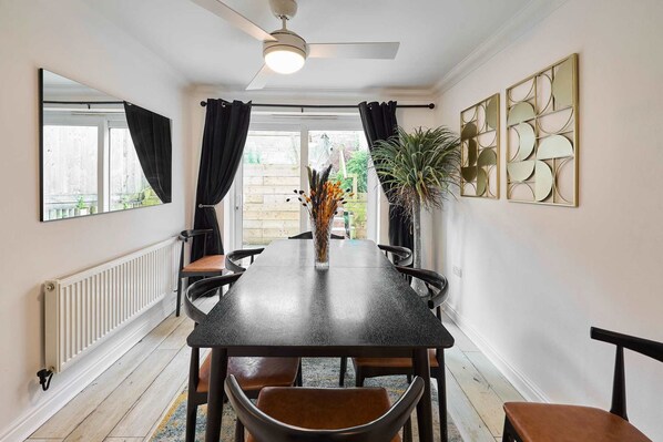 A dining area with a table, chairs, a ceiling fan, a radiator, and decorative wall art.