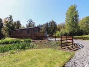 A small wooden cabin with a deck, a pond, and a gravel path. - Butterfly Hut 1 (Preston)