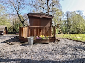 A wooden cabin with a porch, surrounded by gravel and trees. - Butterfly Hut 1 (Preston)