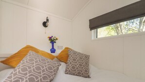 Ein Schlafzimmer mit einem Bett, Kissen, einer Blumenvase, einer Wandleuchte und einem Fenster.