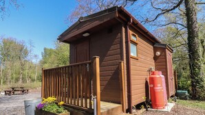 A wooden cabin with a porch, a fire extinguisher, and a picnic table. - Butterfly Hut 2 (Preston)