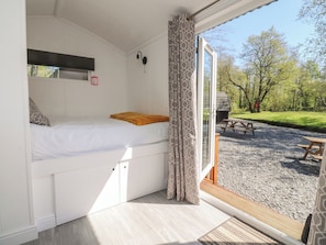 Una stanza con un letto, una finestra con tende e vista su uno spazio all'aperto con un tavolo da picnic.