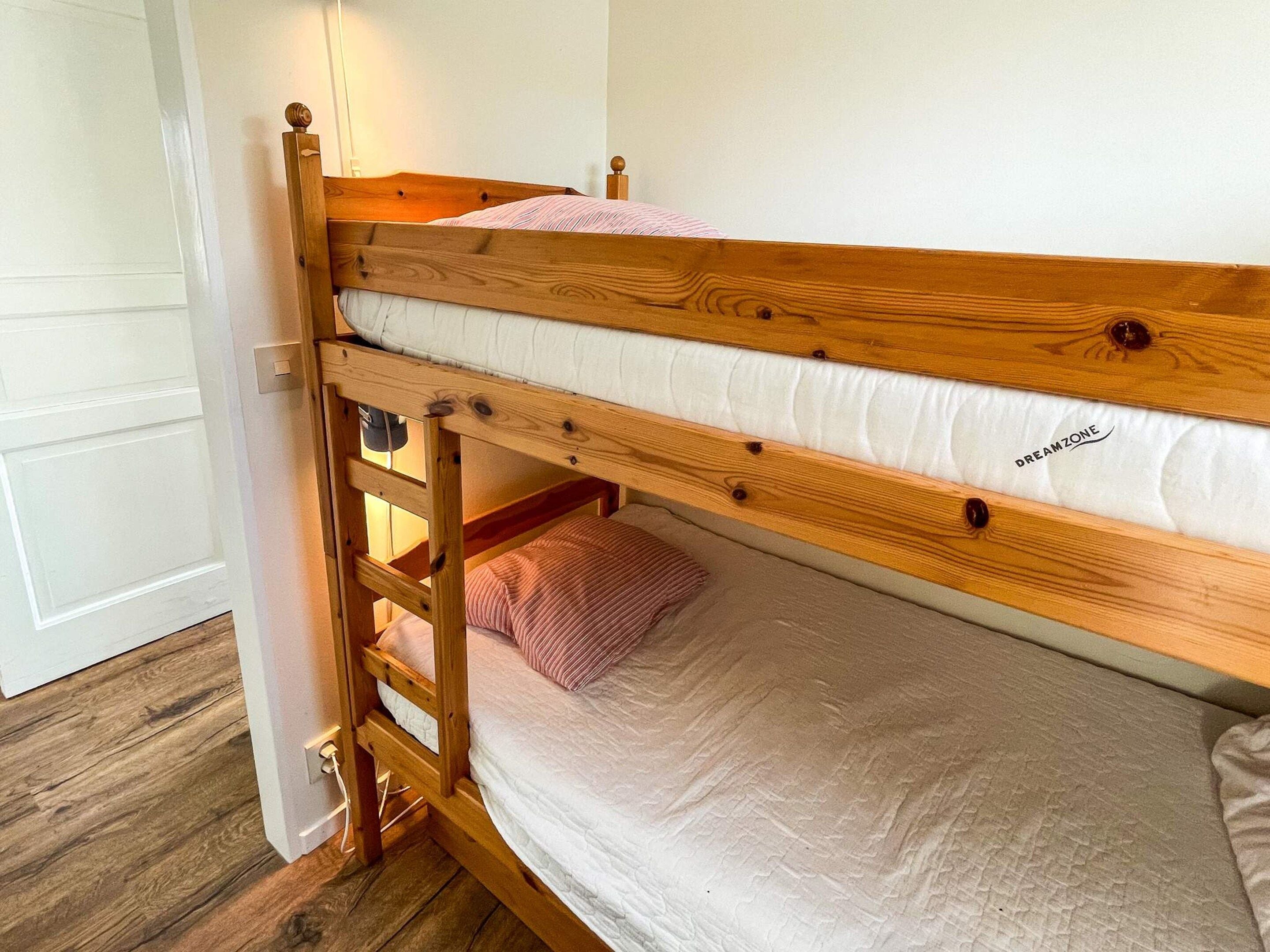Un lit superposé avec une échelle, une porte blanche et un plancher en bois.
