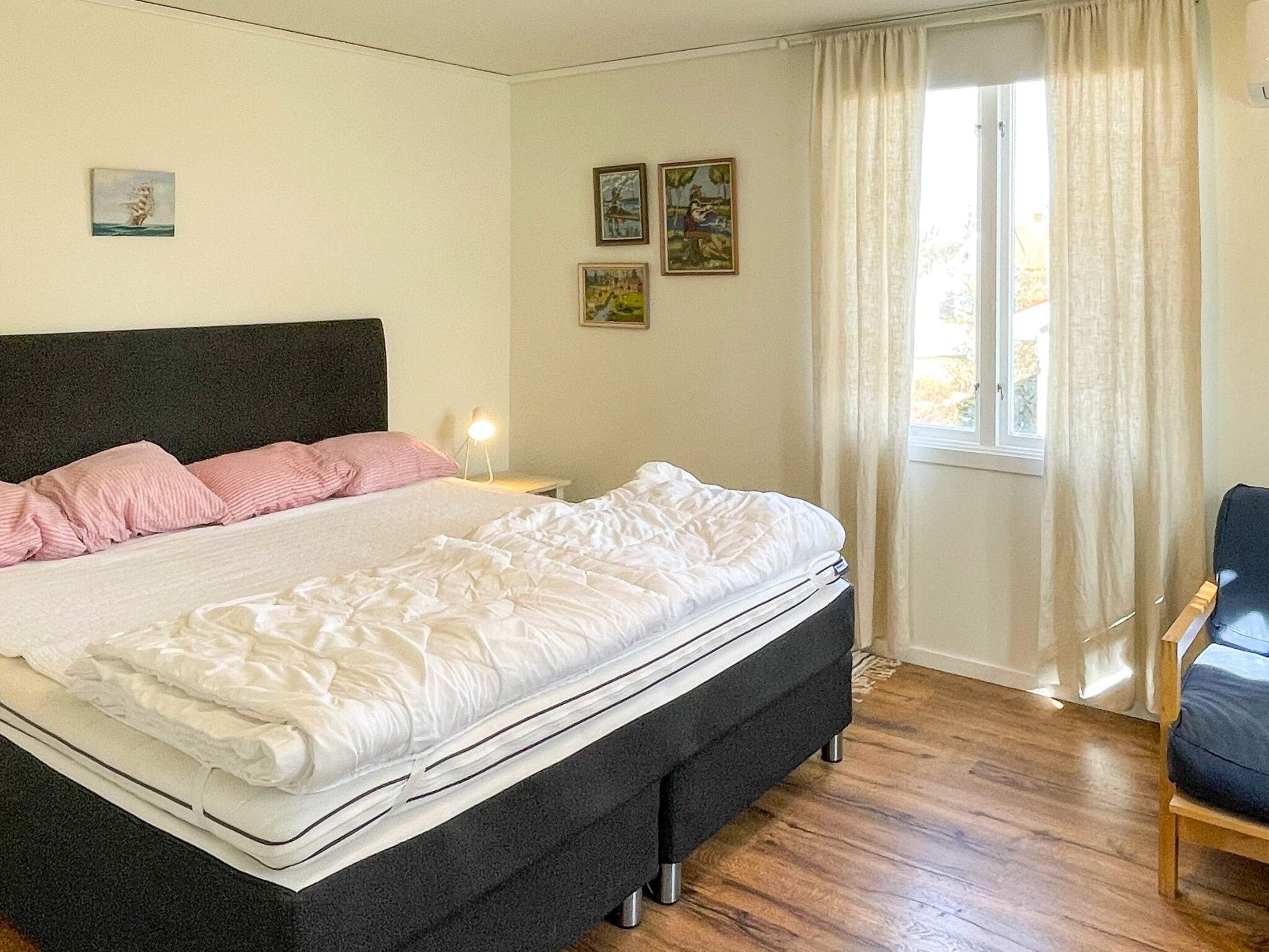 Un dormitorio con cama, mesita de noche, silla y ventana con cortinas.
