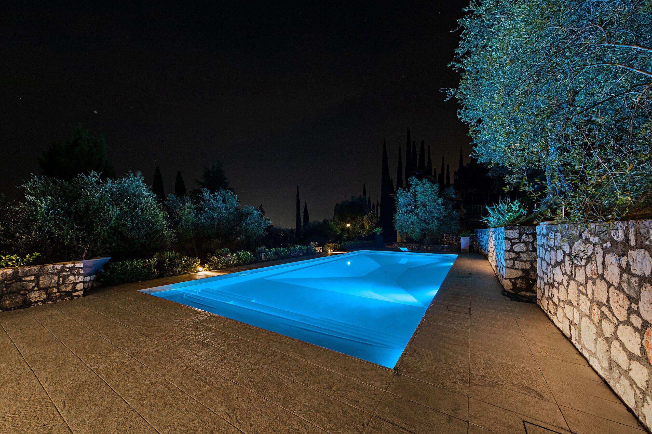 Una piscina con un muro de piedra a un lado y otro, rodeada de árboles y plantas.