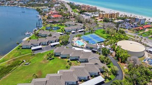 An aerial view of a coastal residential area with houses, a tennis court, and a beach. - Pelican Harbour, Beach Club T2 Condo by RVA (Longboat Key)