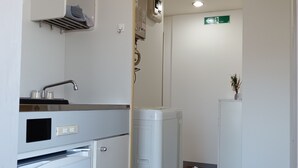 A compact kitchen with a refrigerator, a sink, and a small countertop. There is a wooden floor and a blue mat at the entrance.