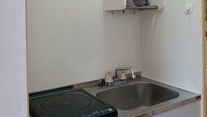 A compact kitchen with a built-in induction cooktop, a stainless steel sink, and a microwave above the sink.