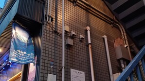A building exterior with tiled walls, visible pipes, and a blue railing.