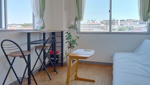 A room with a bed, a desk with a chair, a window with curtains, and a plant.