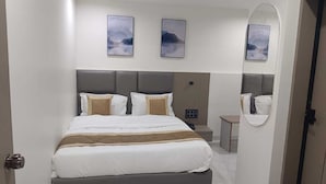 A modern hotel room with a large bed, a bedside table, a mirror, and artwork on the walls. - Hotel Lavit (Ahmedabad)