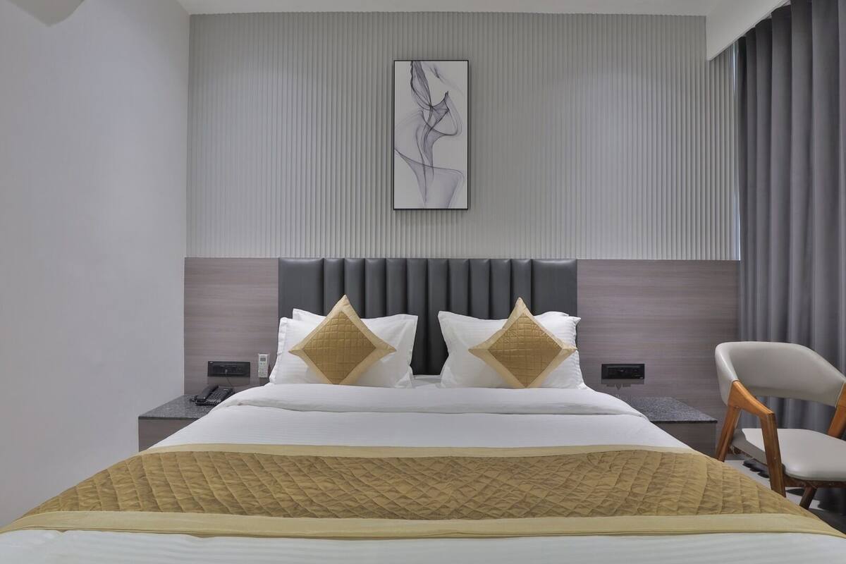 Habitación de hotel moderna con una cama grande, dos almohadones decorativos, un cabecero, una mesita de noche con teléfono y una silla.