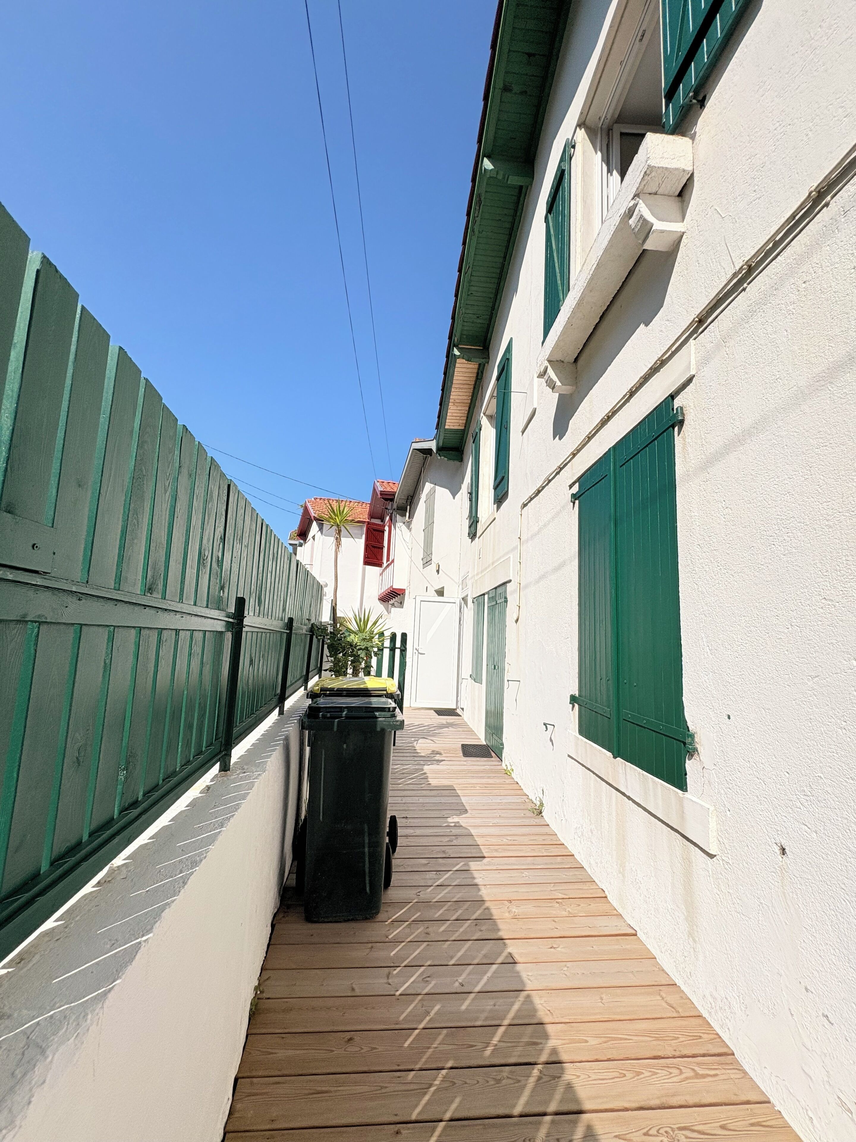 Un estrecho sendero de madera bordeado por edificios blancos con contraventanas verdes y una cerca de madera.