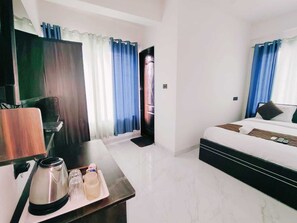 A hotel room with a bed, a desk with a kettle, and a TV. - Hotel Revmantra (Pune)