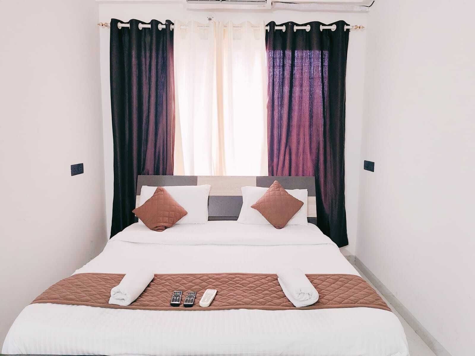 A neatly made bed with a quilted brown bedspread, two pillows, and a set of remote controls on the bed.