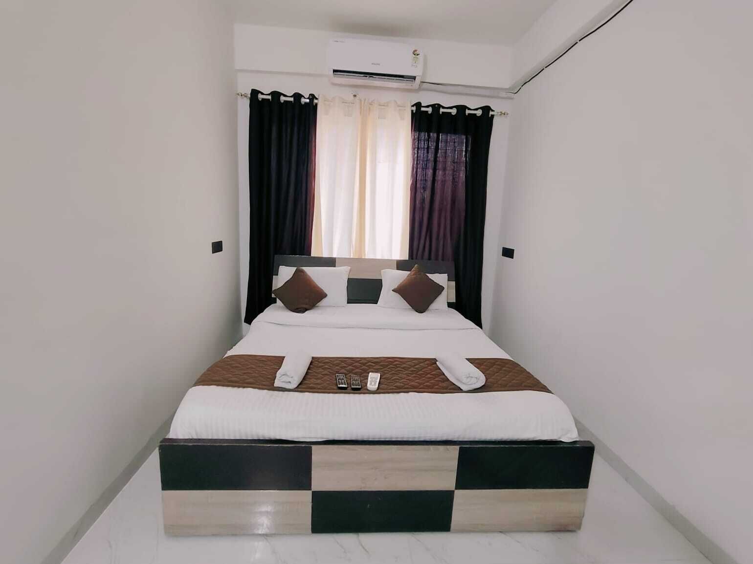 Una cama bien hecha con una base a cuadros, ropa blanca y varias almohadas.