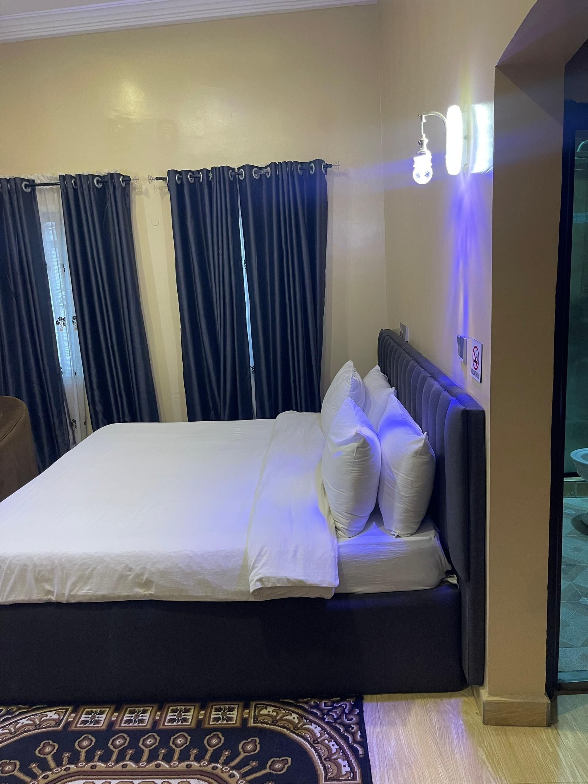 A neatly made bed with white linens, a dark headboard, and a blue patterned rug.