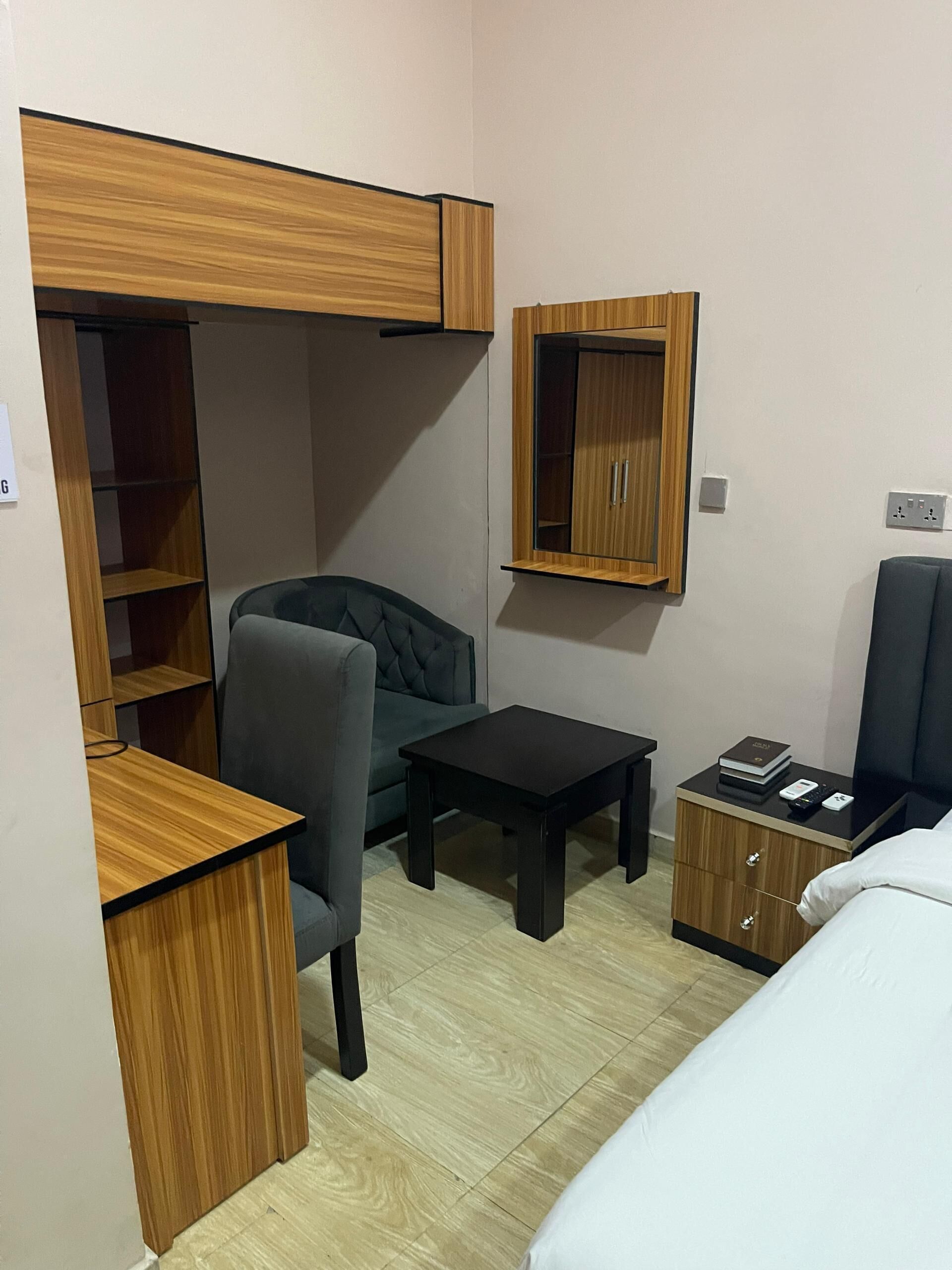 A compact room with a bed, a desk, a chair, a wardrobe, and a small table.