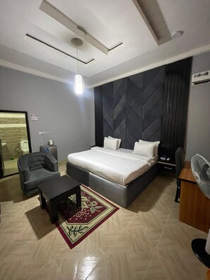 A modern bedroom with a bed, a desk, a chair, and a small table. - DE ROSS HOTEL & SUITES (Uyo)