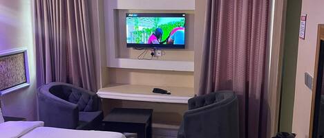 A hotel room with a bed, a desk, a television, and two chairs.