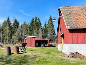 A red barn with a tiled roof, surrounded by a grassy yard and tall trees. - 6 Person Holiday Home in Mellerud (Mellerud)