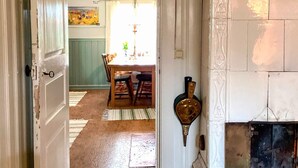 Une porte ouverte donne sur un coin repas où une table est dressée pour deux personnes, agrémentée d’un tapis  à motifs et d’un élément décoratif mural.