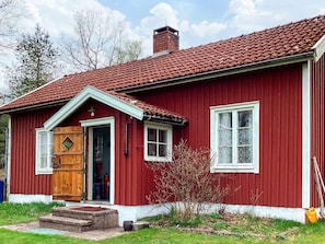 A red wooden house with a tiled roof, a wooden door, and a small garden area. - 6 Person Holiday Home in Mellerud (Mellerud)