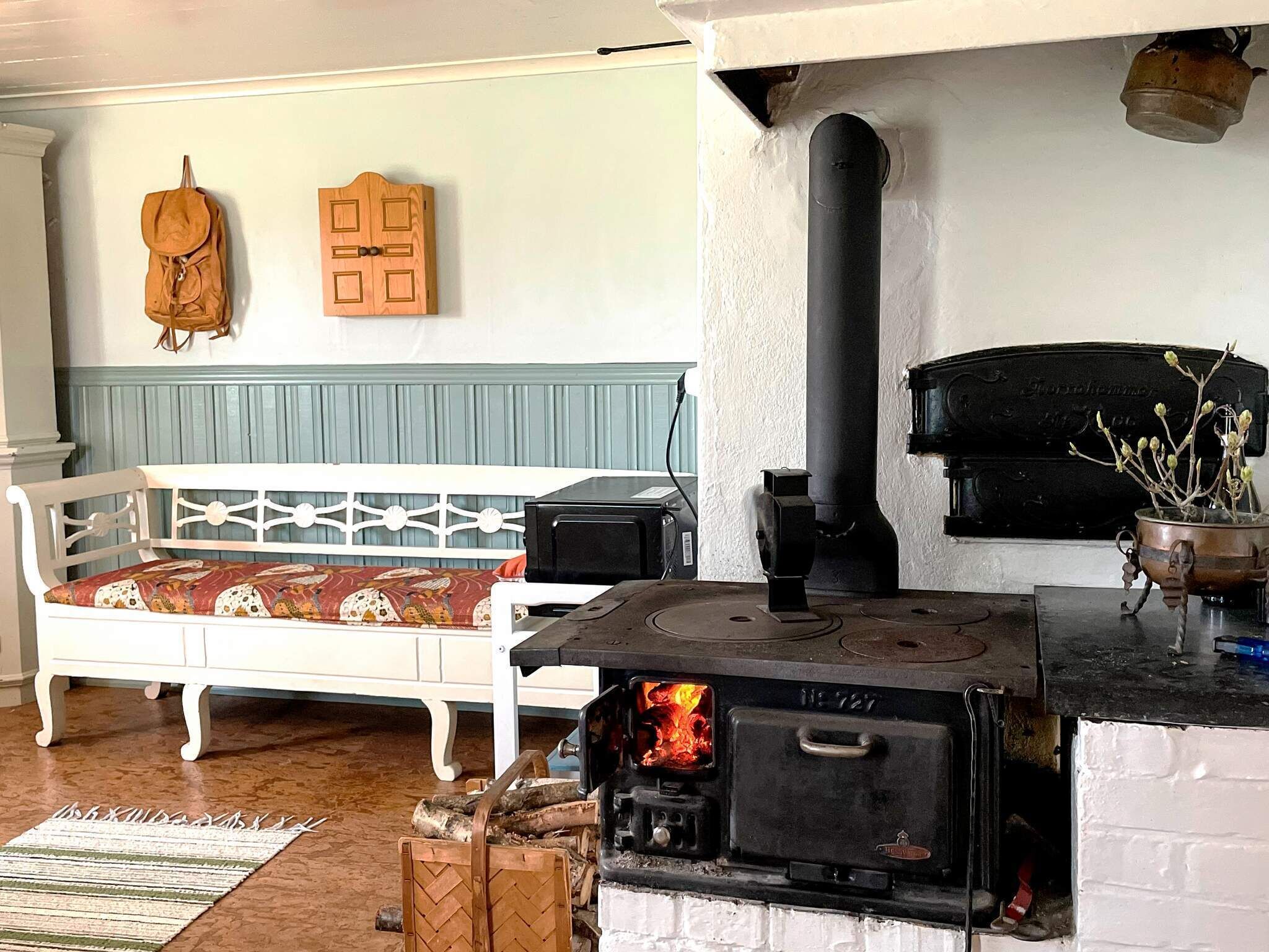 A cozy room with a white sofa, a wood-burning stove, and a hanging coat rack.