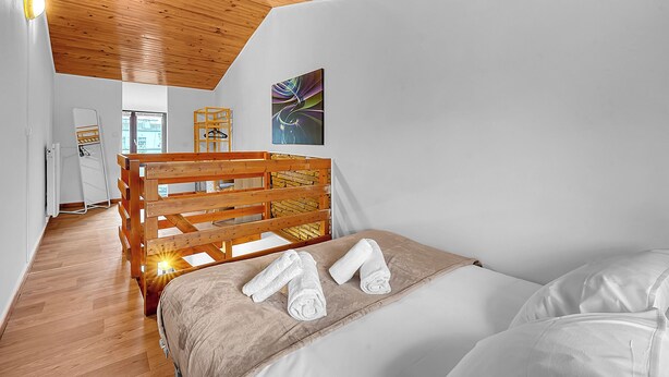 Une chambre avec un lit superposé en bois, un mur blanc, un plafond en bois et un tableau.