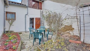Une cour avec une table et des chaises, un petit arbre et un mur en briques.