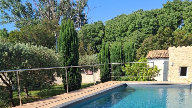 Una piscina rectangular con agua azul cristalina, rodeada por una terraza de madera y barandales de metal.