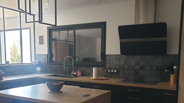 A modern kitchen with a central island, dark cabinetry, and a large window.