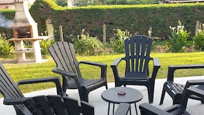 Outdoor seating with Adirondack chairs and a small round table, surrounded by a well-maintained garden and a stone structure in the background.