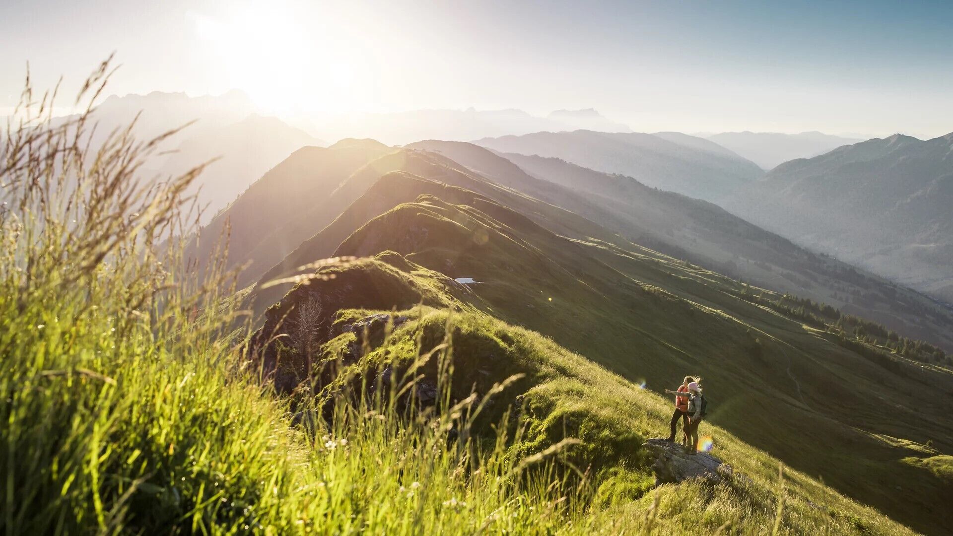 A mountainous landscape with a person standing on a grassy hill.