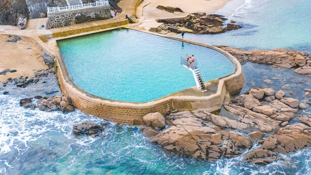 An aerial view of a swimming pool surrounded by rocky terrain and the ocean.