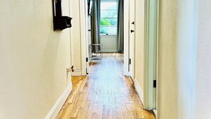 A hallway with wooden flooring, white walls, and a door leading to a room with a window.