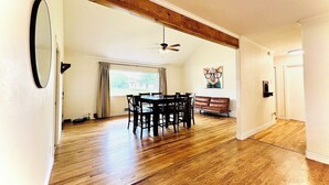 A spacious dining area with a wooden floor, a dining table with chairs, a ceiling fan, and a painting on the wall.