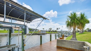Un muelle de madera con un toldo, una palmera y una masa de agua.